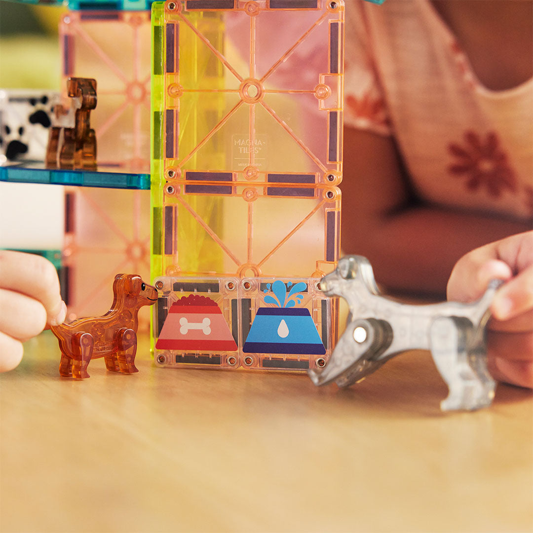 Twee puppyfiguren bij magnetische tegels met afbeeldingen van een voer- en waterbak.