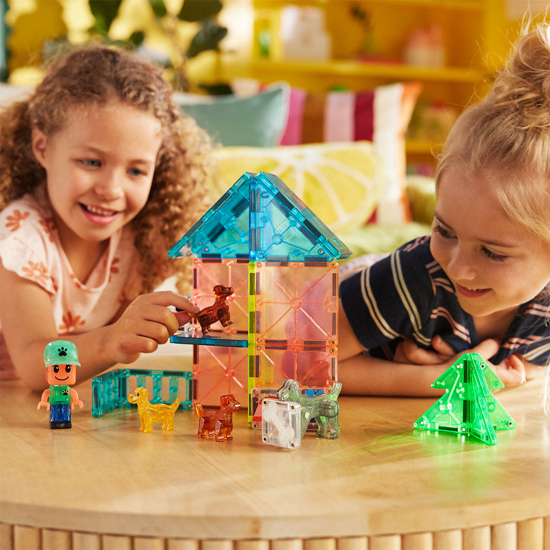 Twee kinderen spelen met de Magna-Tiles Puppy Park bouwset op een houten tafel.