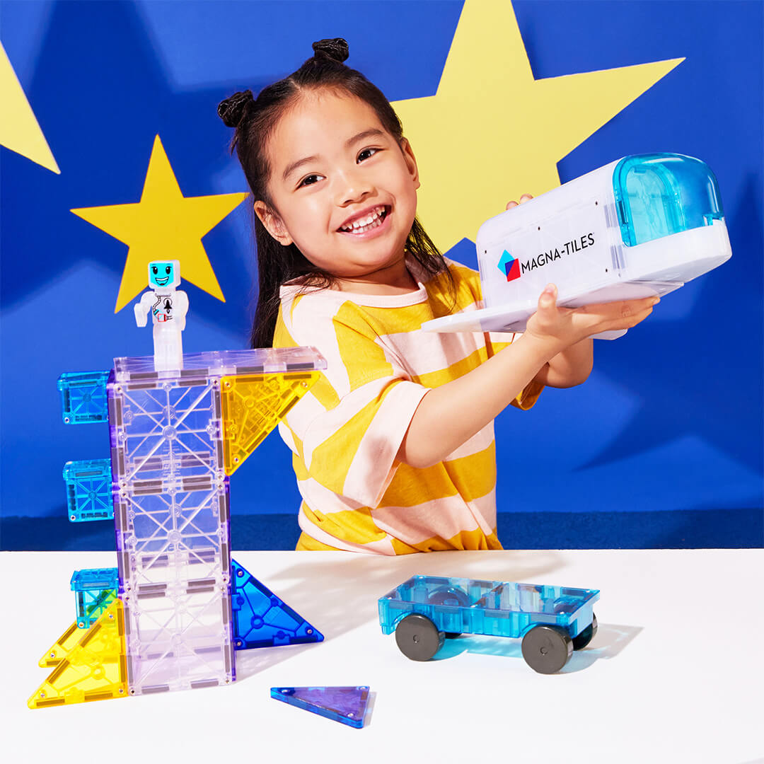 Een lachend meisje speelt met een Magna-Tiles Space magnetische tegels ruimte shuttle en een lanceerplatform.