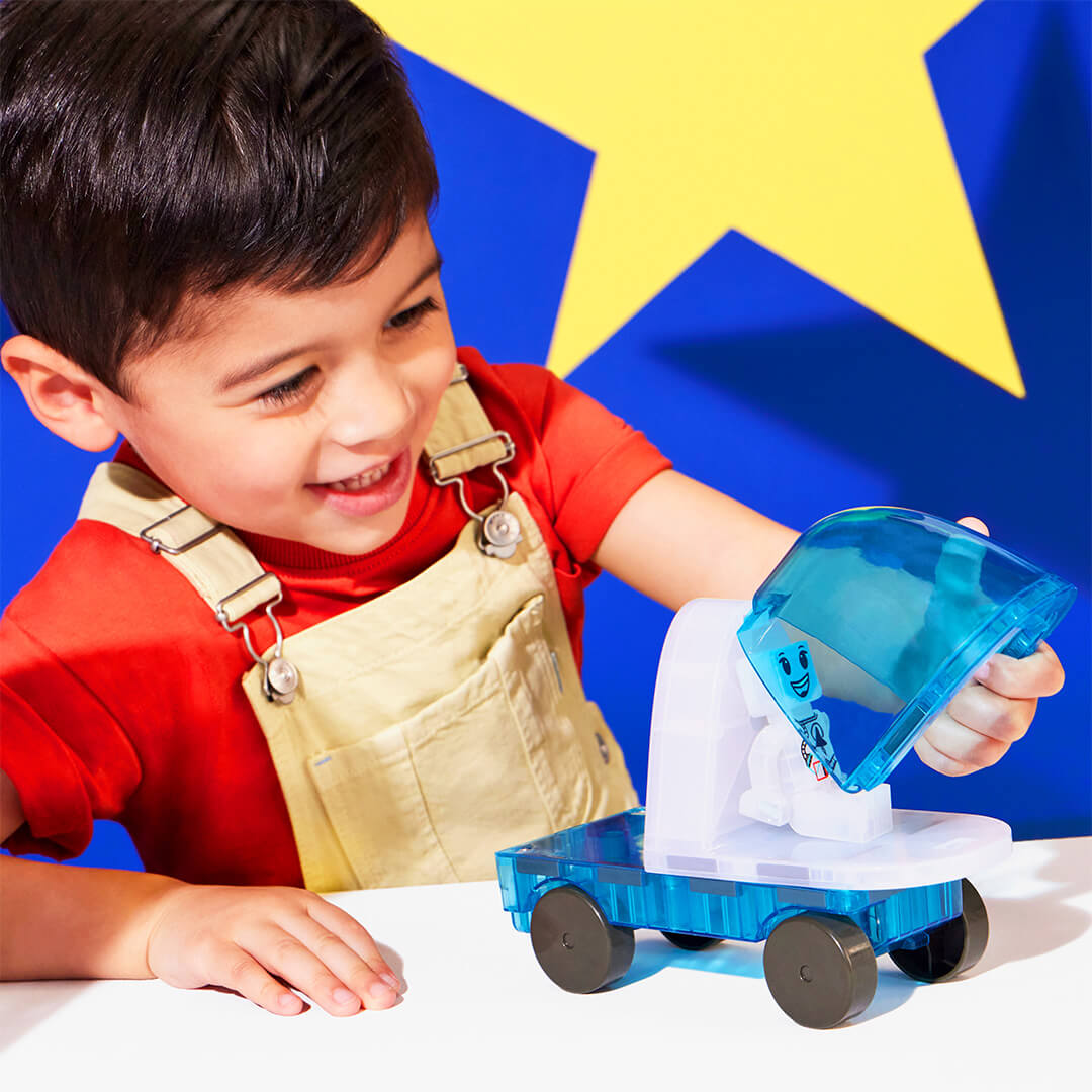 Een lachende jongen speelt met een Magna-Tiles Space magnetische tegels voertuig en opent de cockpit.