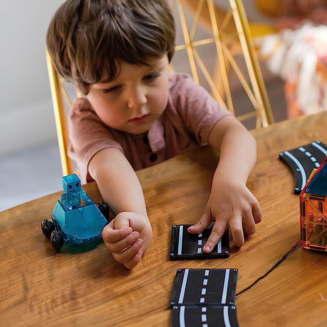 Een kind speelt met Magna-Tiles magnetische wegtegels en een blauwe speelgoedauto op een houten tafel.