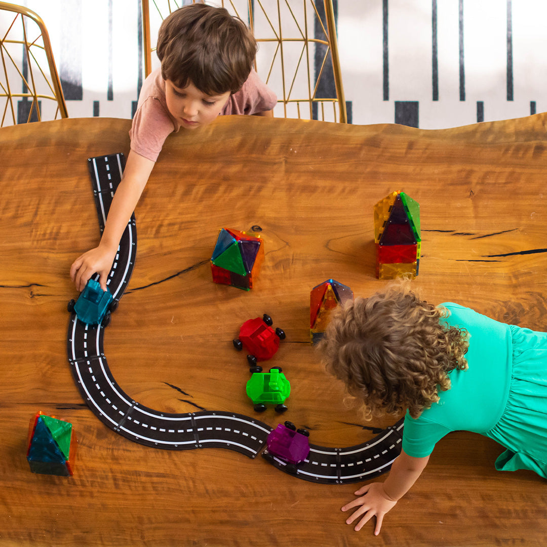Twee kinderen spelen met Magna-Tiles magnetische wegtegels en bouwblokken op een houten tafel.