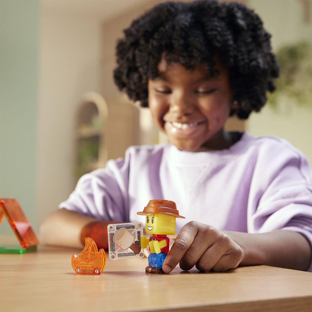 Een kind speelt met het Magna-Tiles Camp Out figuurtje dat een marshmallow roostert boven een kampvuur.