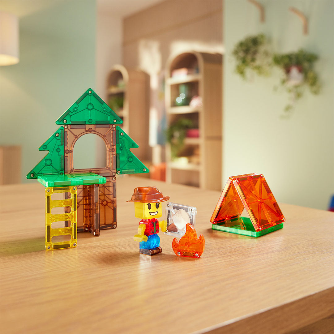 De Magna-Tiles Camp Out magnetische bouwset met een boomhut, een tent, een figuurtje en een kampvuur op een houten tafel.