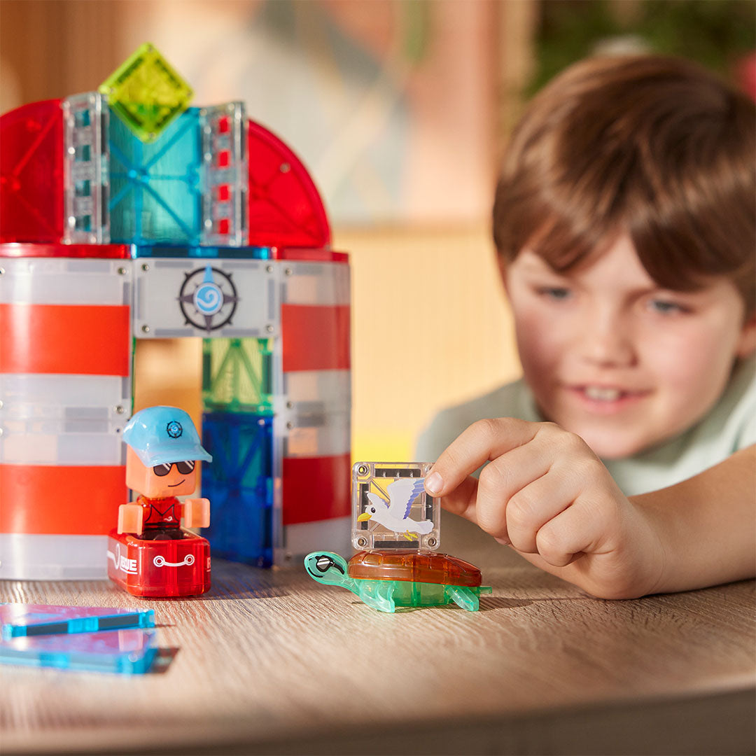 Een jongen speelt met de Magna-Tiles Lighthouse Rescue bouwset, met een figuur, schildpad en vuurtoren.
