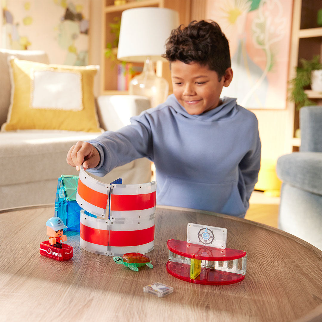 Een jongen bouwt aan de Magna-Tiles Lighthouse Rescue bouwset met magnetische tegels op een houten tafel.