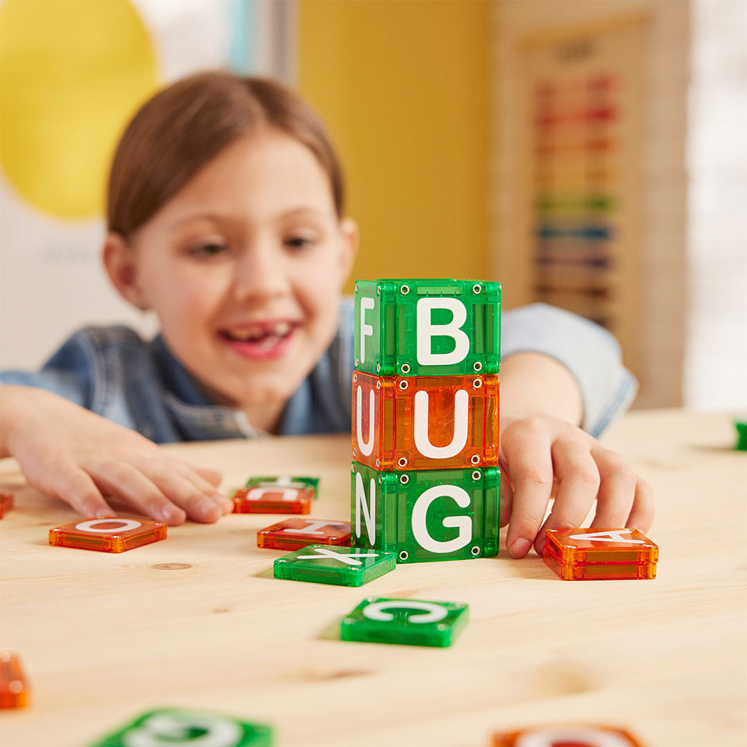 Een meisje speelt met Magna-Tiles magnetische lettertegels en heeft 'FUN' gestapeld op een houten tafel.