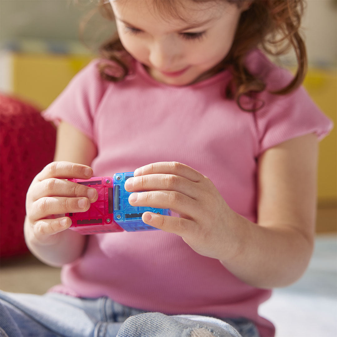Close-up van kinderhanden die twee Magna-Tiles magnetische bouwblokjes aan elkaar klikken.
