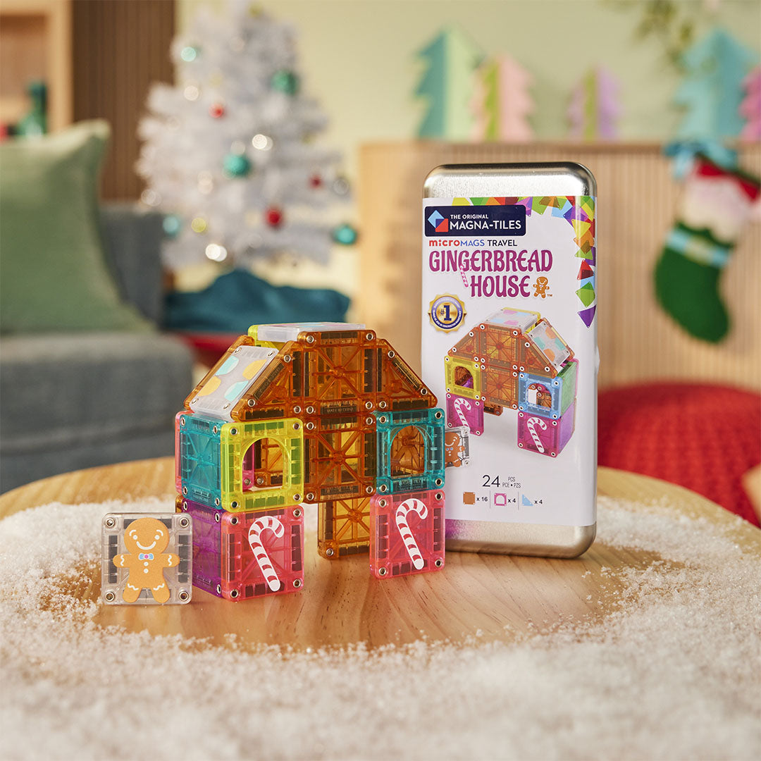 Een gebouwd peperkoekhuis van Magna-Tiles magnetische tegels staat naast de productverpakking op een besneeuwde tafel.