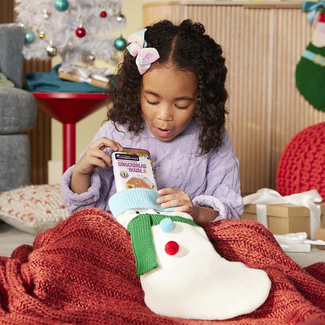 Een kind haalt de Magna-Tiles MicroMags Travel Gingerbread House bouwset verpakking uit een kerstsok.