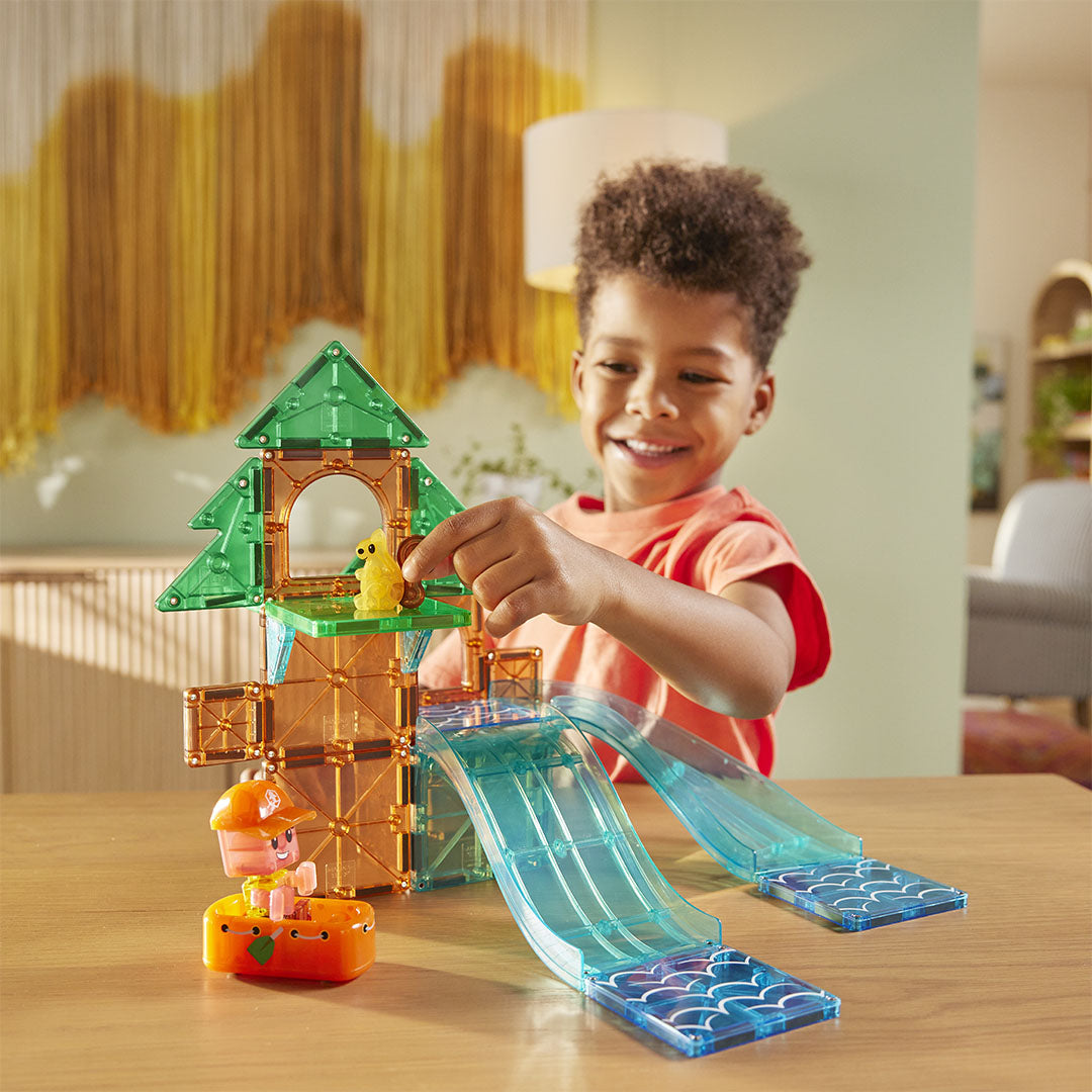 Een lachend kind speelt met de Magna-Tiles Raging Rapids bouwset, een boomhut met glijbanen en een eekhoorn.