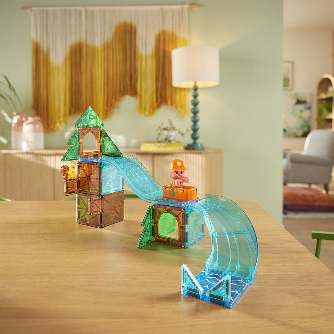 De Magna-Tiles Raging Rapids bouwset toont een boomhut met glijbanen, een figuur in een bootje en een eekhoorn op een tafel.
