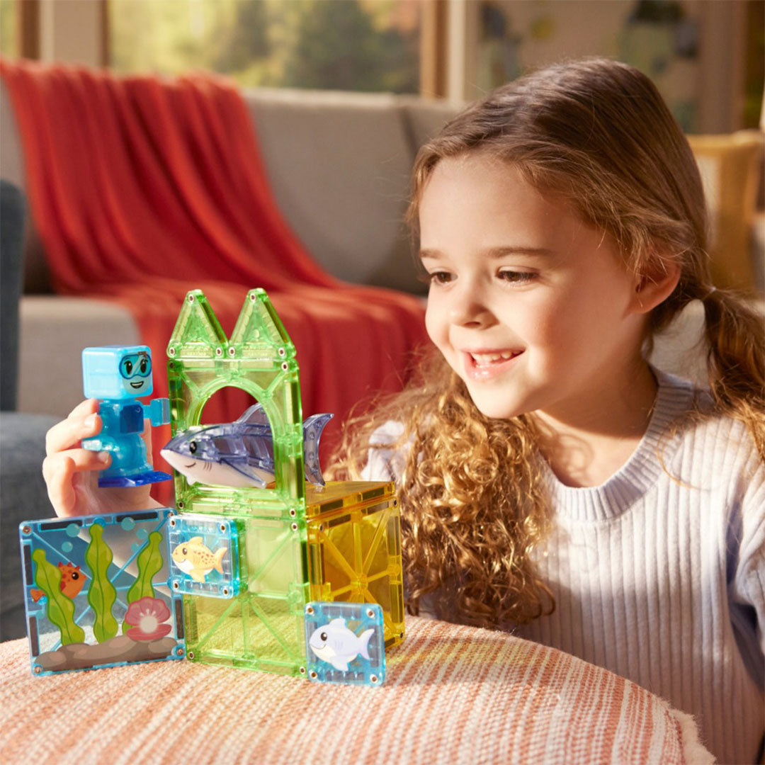 Een lachend meisje speelt met de Magna-Tiles Shark Dive magnetische tegels bouwset, inclusief een duiker en haai.