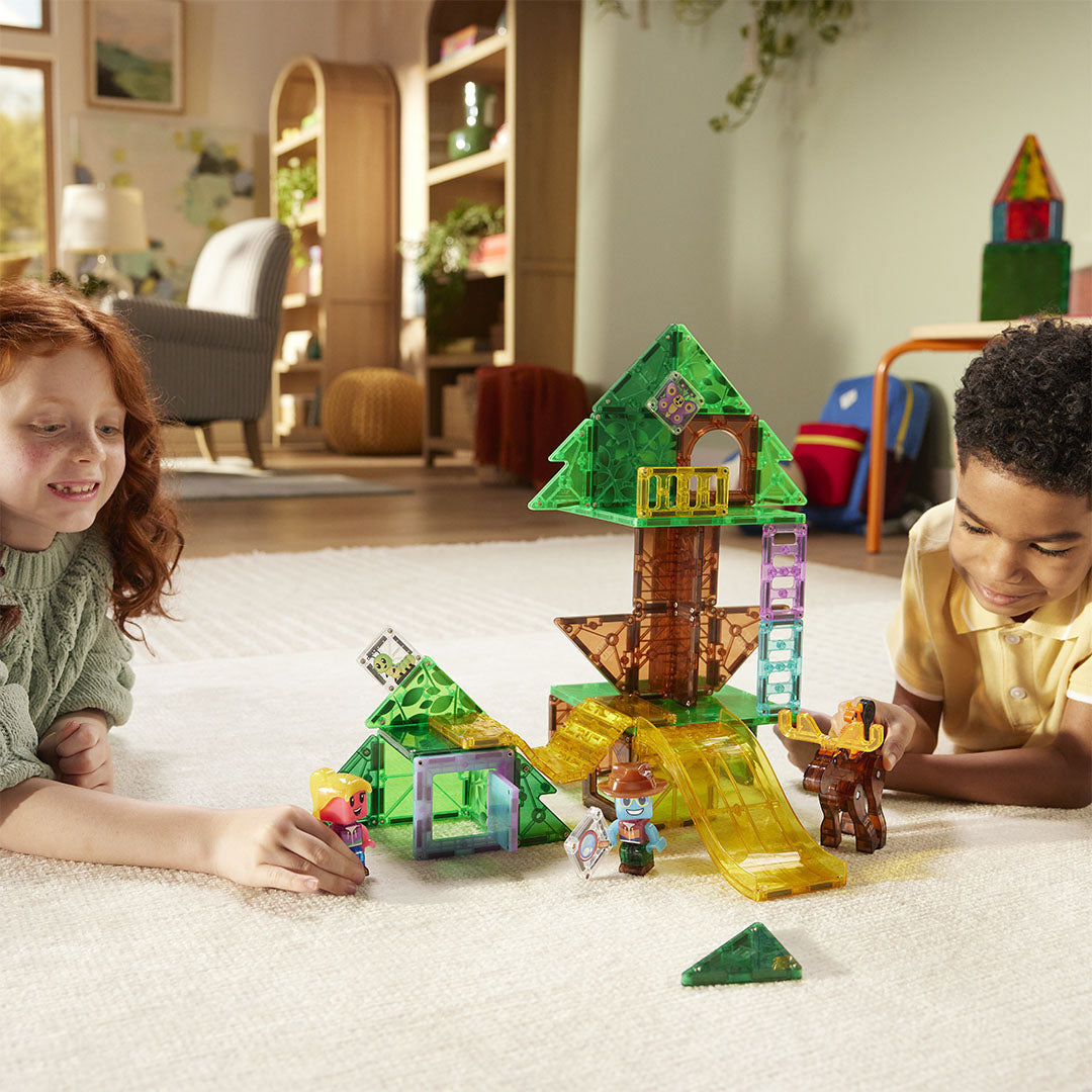 Twee kinderen spelen op de grond met de Magna-Tiles Treetop Adventure magnetische tegels bouwset, die een boomhut voorstelt.