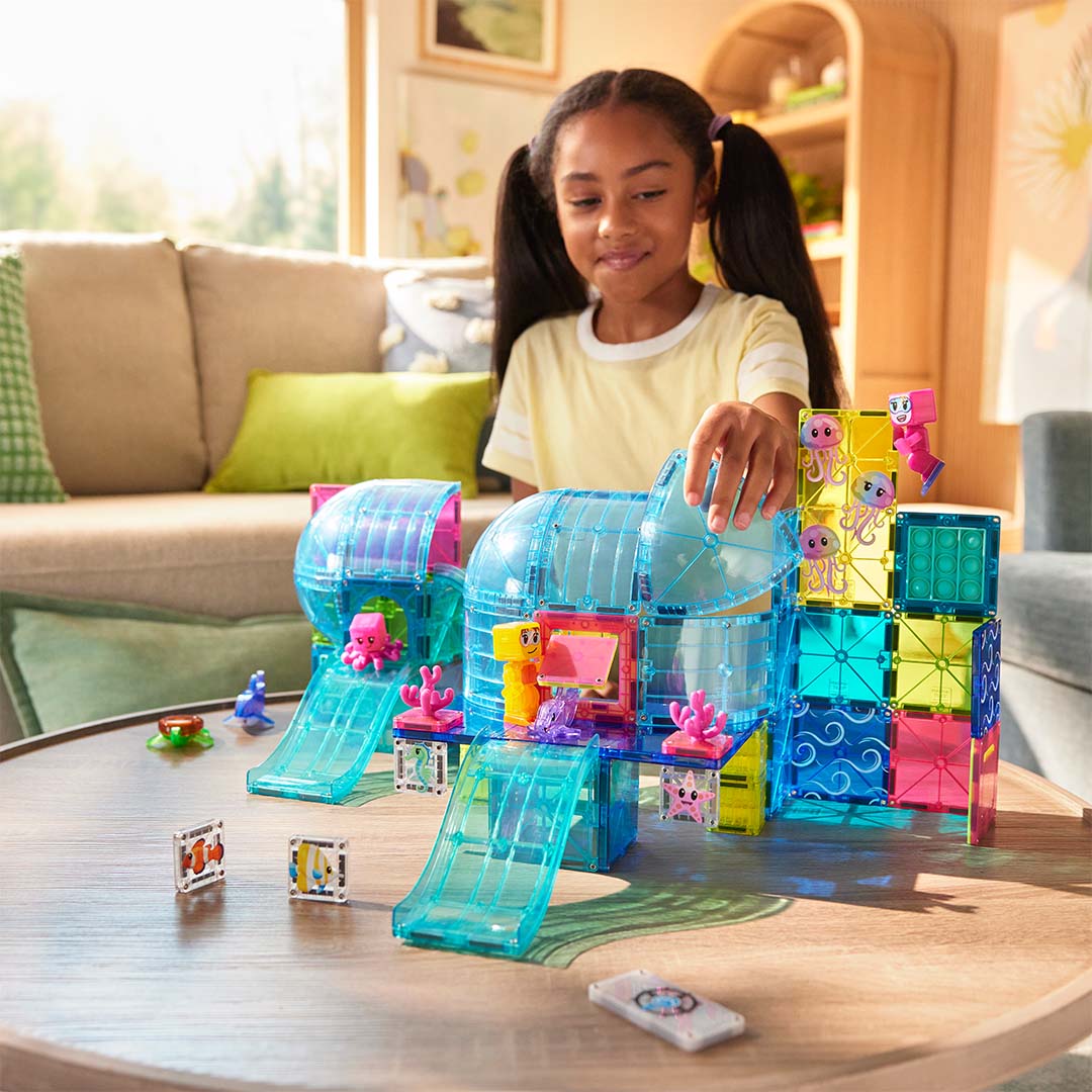 Een meisje speelt met de Magna-Tiles Undersea Adventure bouwset, die een onderwaterwereld van magnetische tegels en zeedieren vormt.