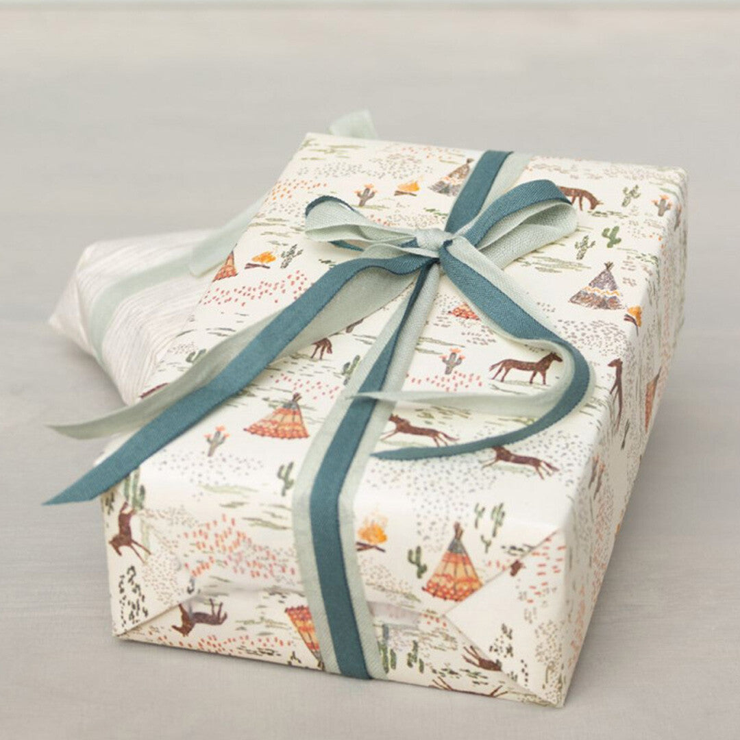 Een ingepakt cadeau met Maileg inpakpapier met paarden en tipi's, versierd met een blauwgroen lint.
