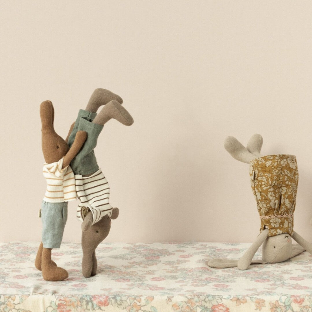 Drie Maileg knuffelkonijnen doen handstanden op een bloemig tafelkleed.