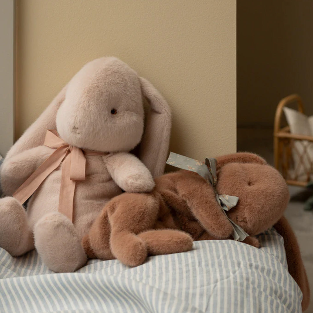 Twee Maileg pluchen knuffelkonijnen, een roze en een bruine, liggen op een gestreepte deken.