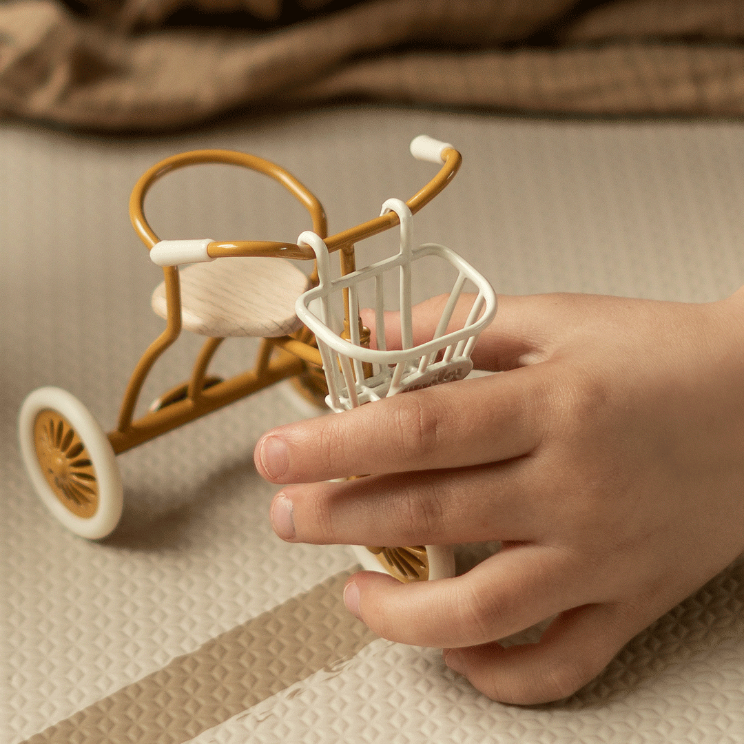 Een kinderhand houdt een Maileg driewieler vast met het witte fietsmandje aan het stuur.