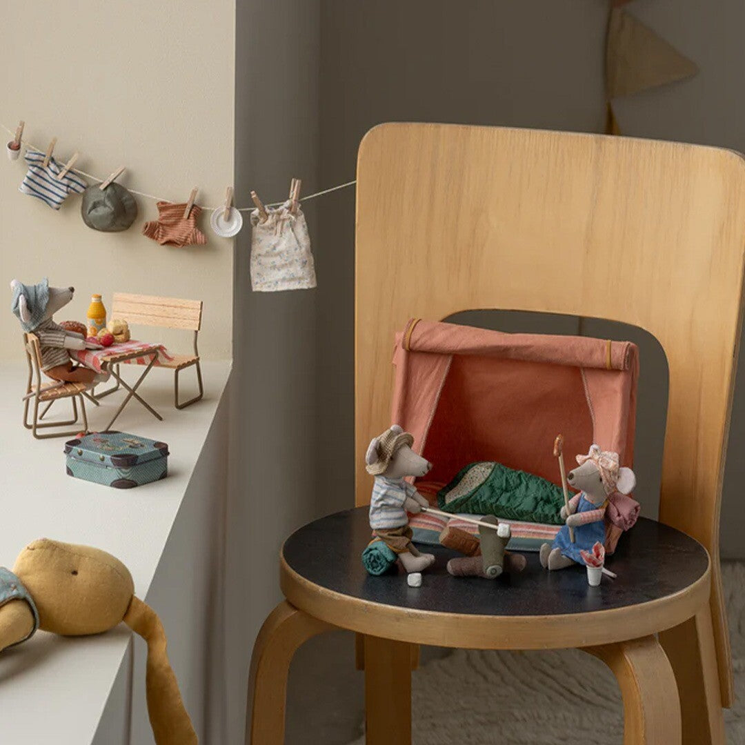Twee Maileg muizenpoppen kamperen bij de rode stoffen tent op een kruk, met een waslijn op de achtergrond.
