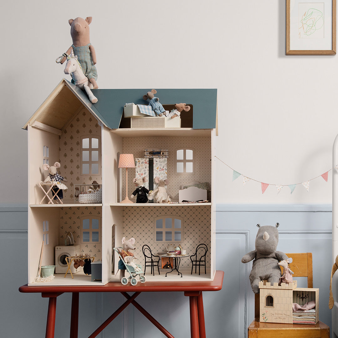 Maileg houten poppenhuis met muizenfiguren en meubels, staand op een rode tafel in een kinderkamer.