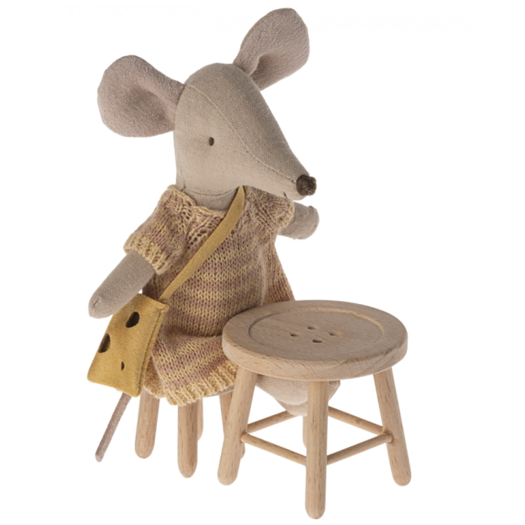 Een Maileg speelgoedmuisje met een kaasvormige tas staat naast een houten poppenhuis krukje.