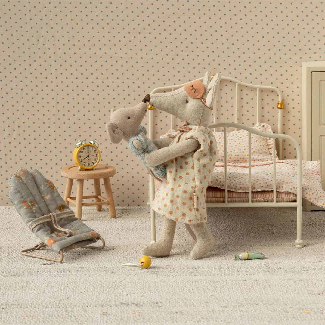 Maileg poppenhuis scène met een muizenpop die een babymuis vasthoudt naast het gebloemde wipstoeltje en een bed.