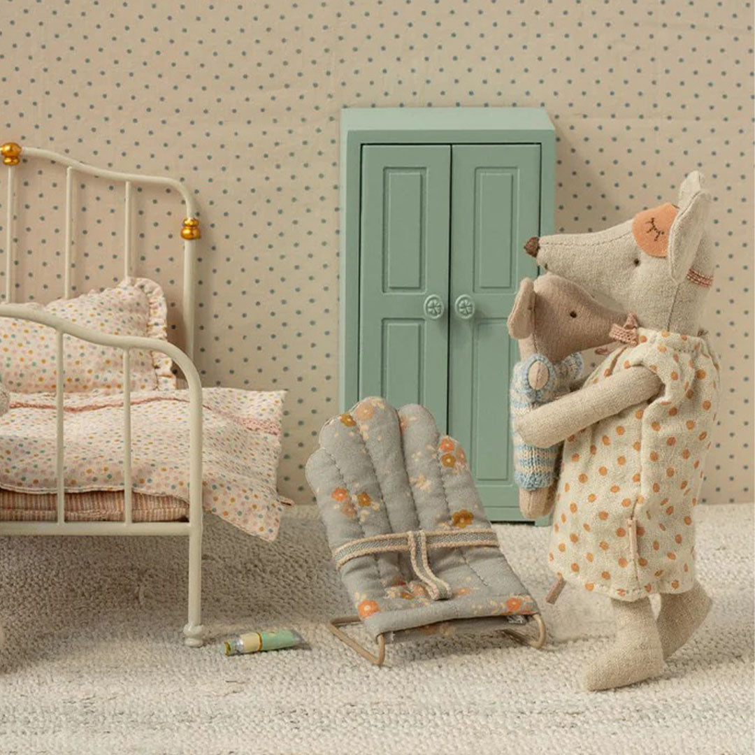 Maileg poppenhuis scène met een muizenpop die een babymuis vasthoudt naast het gebloemde wipstoeltje en een kledingkast.