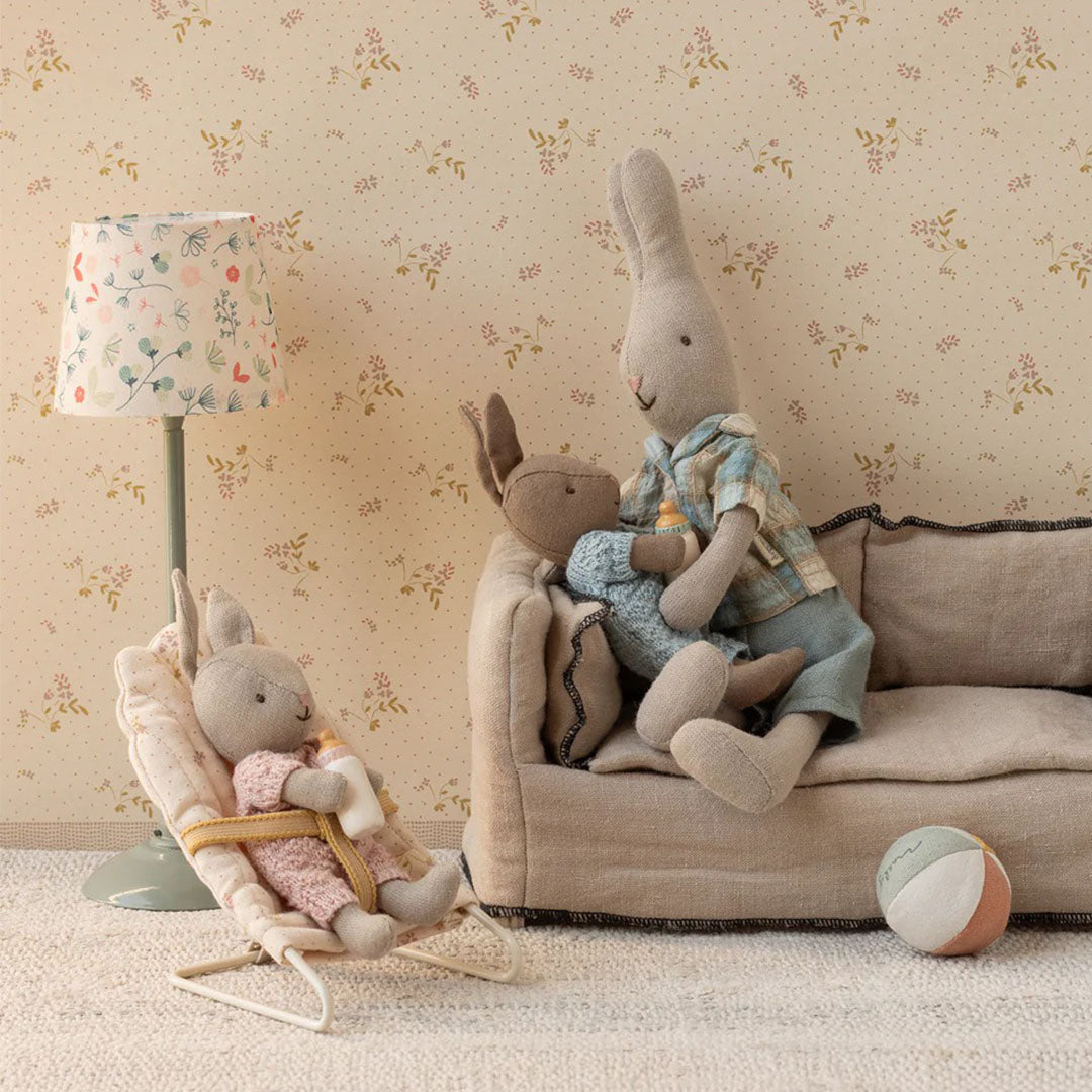 Maileg poppenhuis wipstoeltje met een konijnenpopje dat een flesje krijgt in een miniatuur woonkamer.