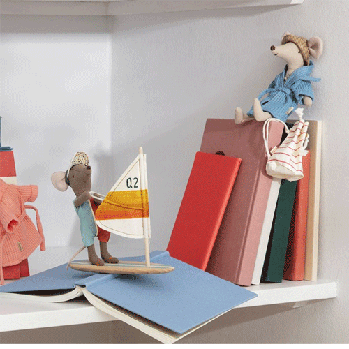 Twee Maileg muis poppen, waarvan één in een blauwe badjas, spelen op een plank met boeken en een zeilboot.