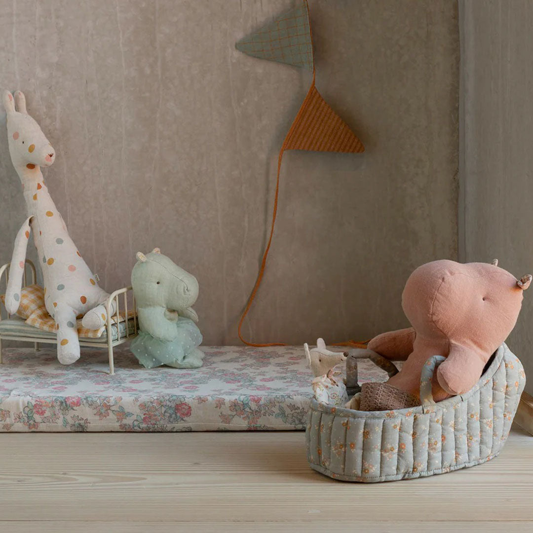 Maileg poppenreiswieg met een roze nijlpaard knuffel erin, staand op een speelmat met andere knuffels.