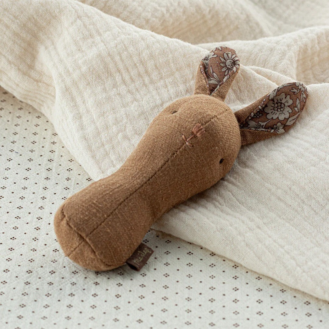Maileg babyspeelgoed rammelaar in de vorm van een bruin konijn, liggend op een lichte deken.