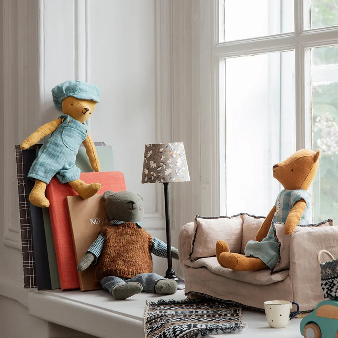 Drie Maileg knuffelberen in een kamer, zittend op boeken, een vensterbank en een minibankje.