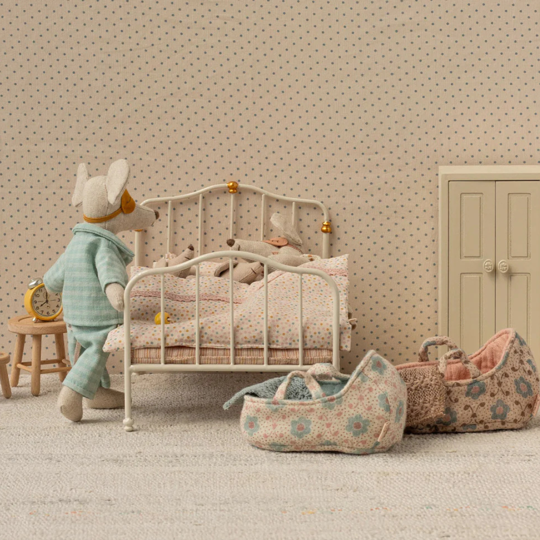 Maileg muis in pyjama naast een bed met een bloemige poppenreiswieg op de vloer.