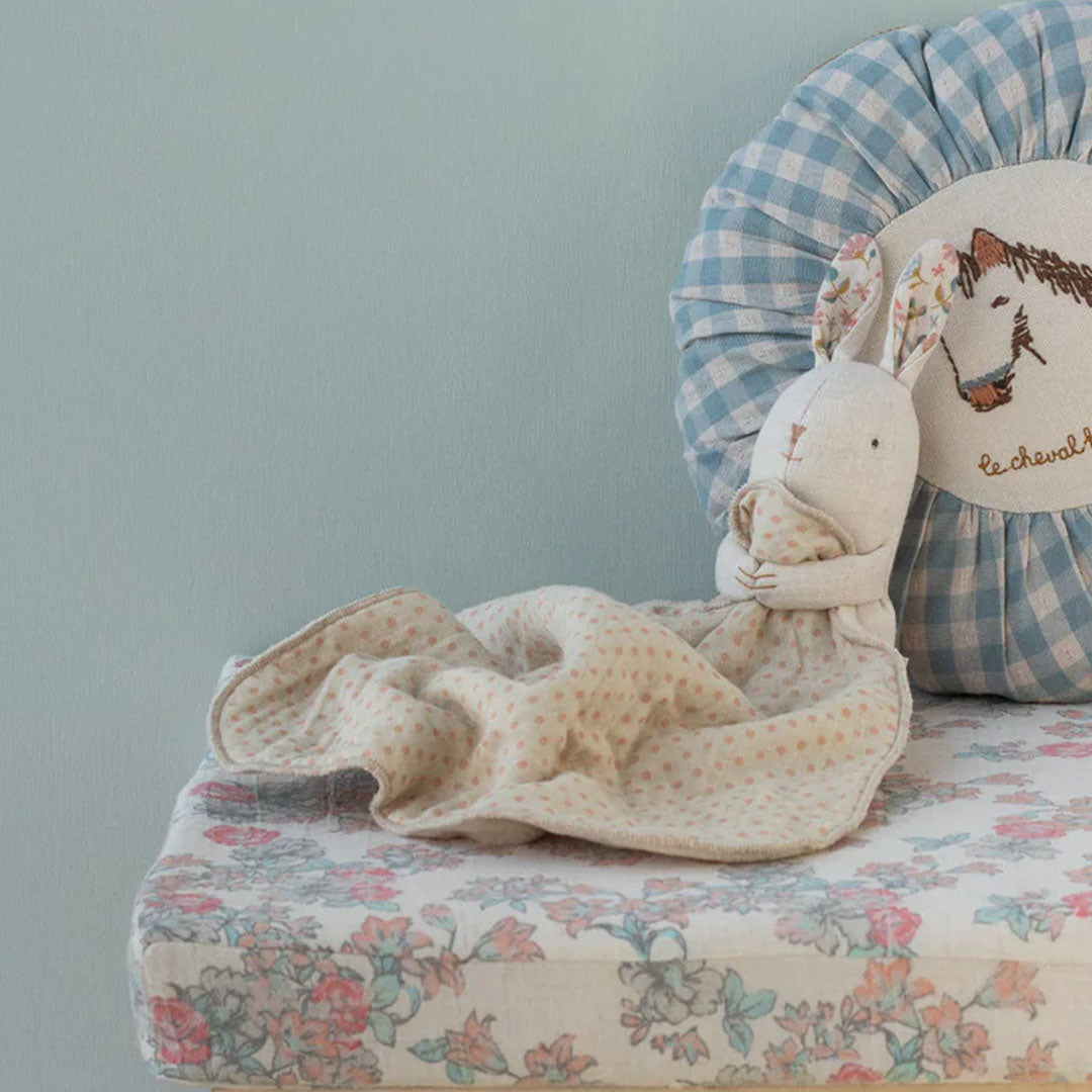 Maileg knuffelkonijn met gebloemde oren en een beige knuffeldoek met stippen op een bloemig kussen.