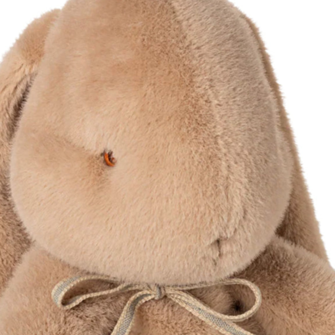 Detailopname van het beige pluchen knuffelkonijn, met focus op het hoofd en het strikje.
