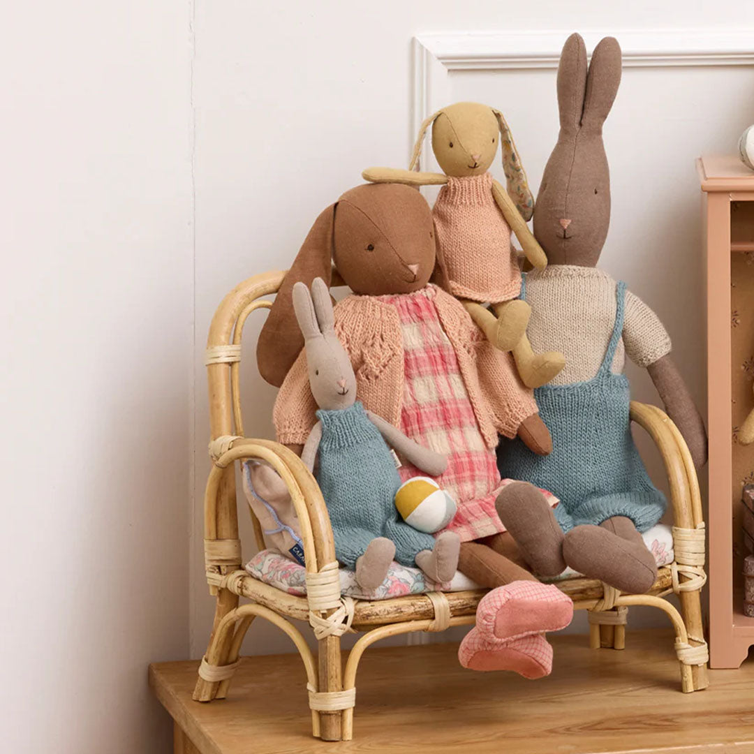 Een groep Maileg knuffelkonijnen in diverse outfits zittend op een rotan stoel.
