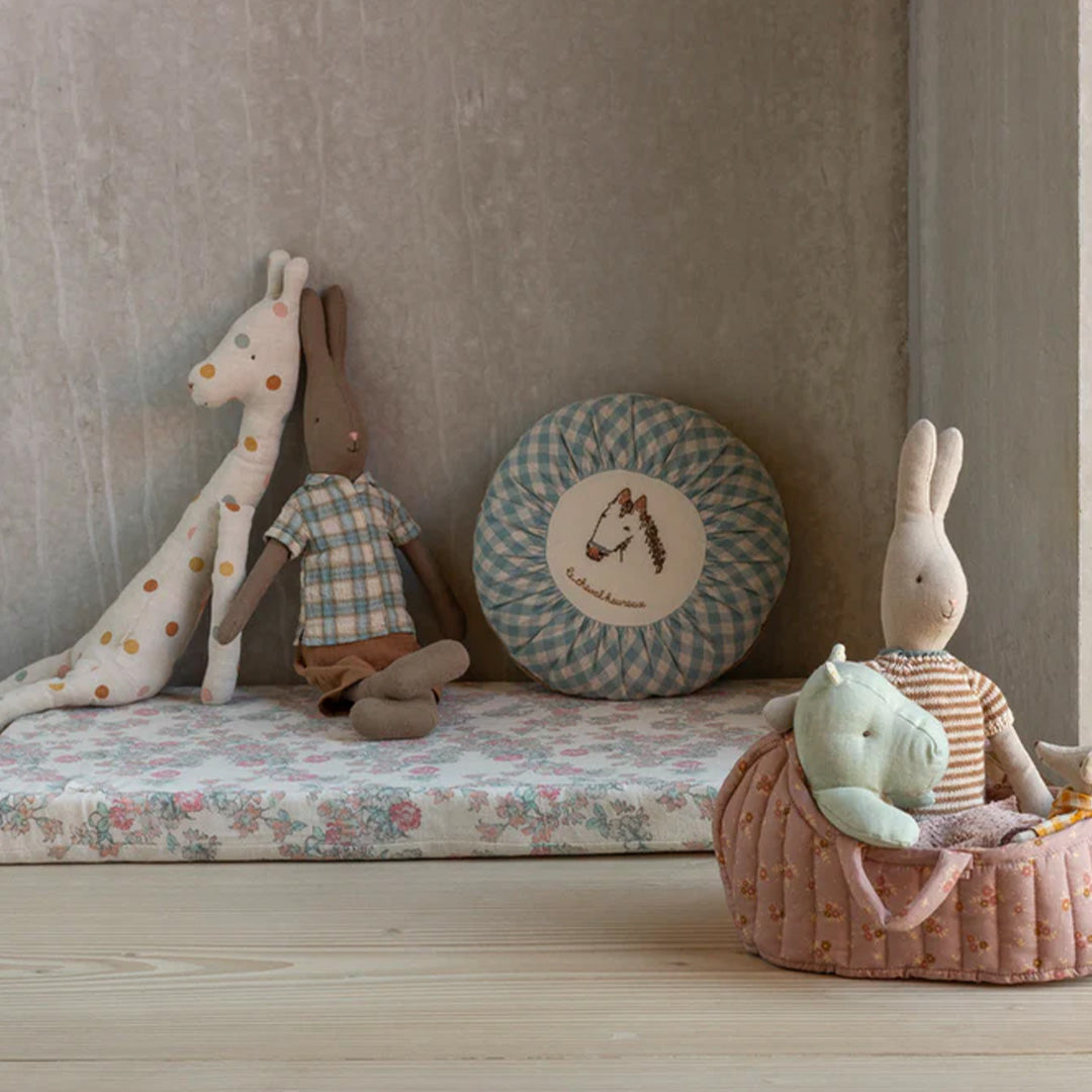 Verschillende Maileg knuffels, waaronder konijnen en een giraffe, op een bloemenmat.