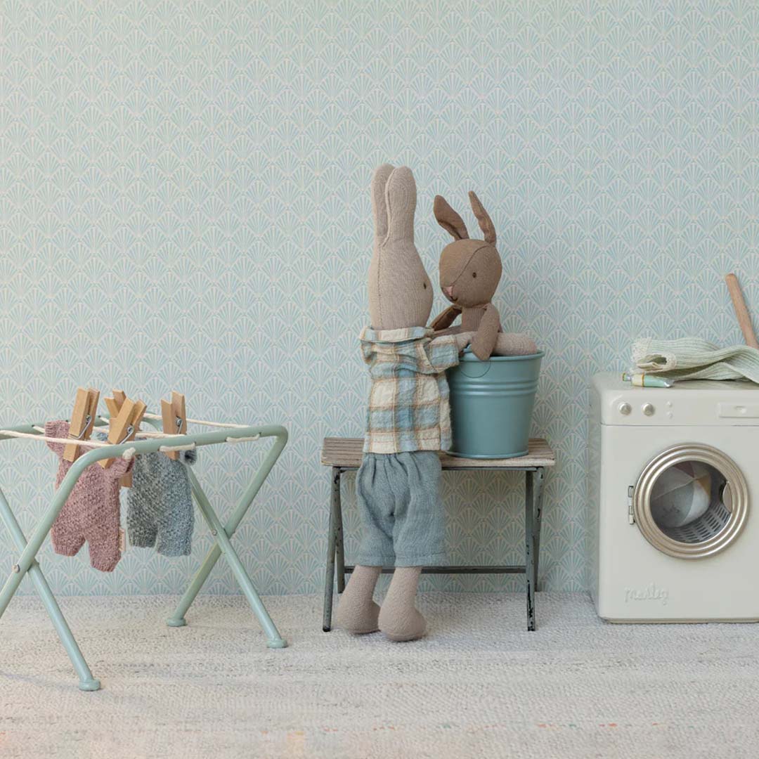 Twee Maileg knuffelkonijnen in een miniatuur wasruimte met een wasrek en wasmachine.