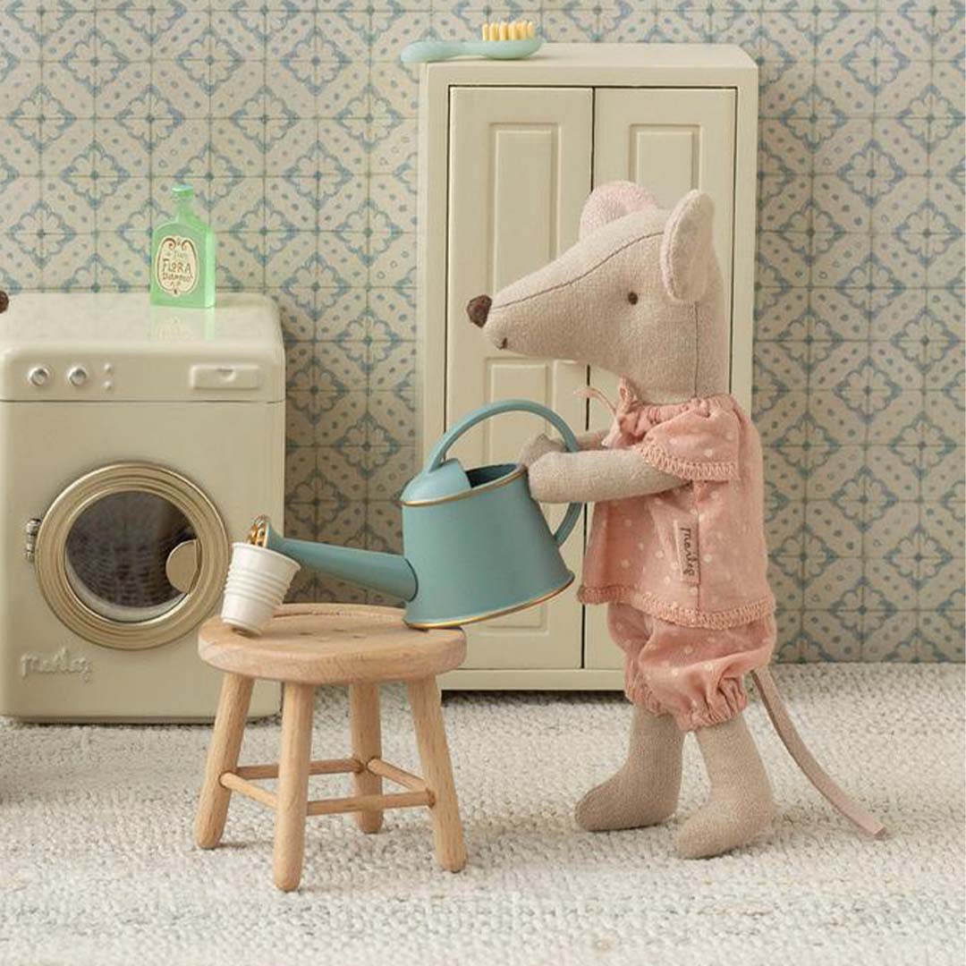 Maileg knuffelmuis grote zus in roze pyjama giet water met een blauwe gieter in een miniatuur badkamer.