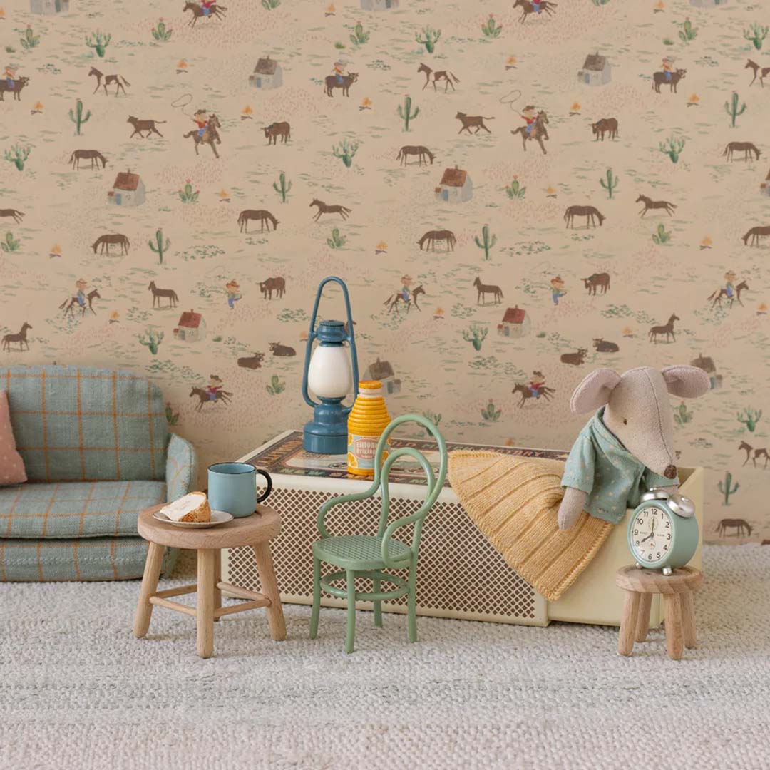 Maileg knuffelmuis in blauwe pyjama staand in een miniatuurkamer met meubels en een cowboy-thema behang.