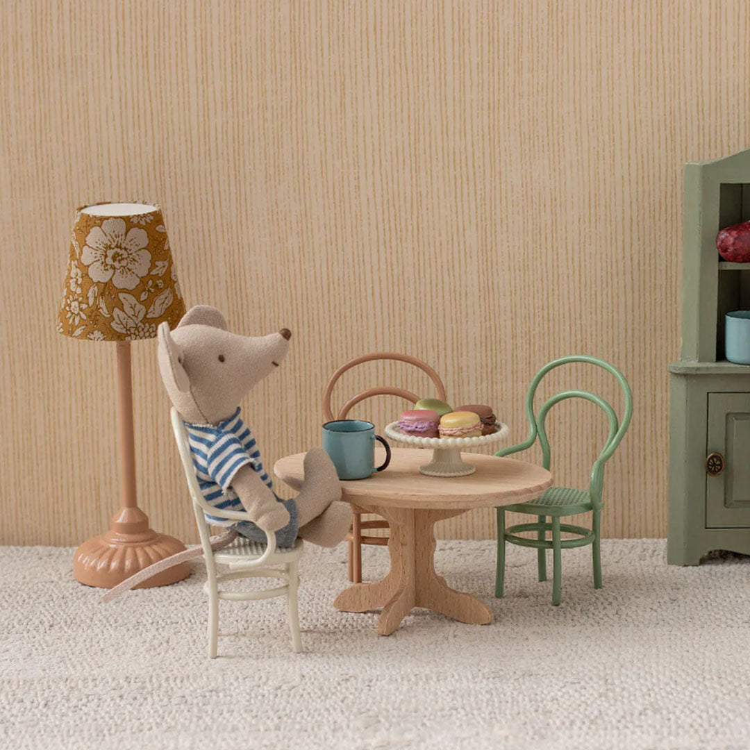 Maileg muispop zit aan de houten poppenhuis eettafel met macarons en een beker.