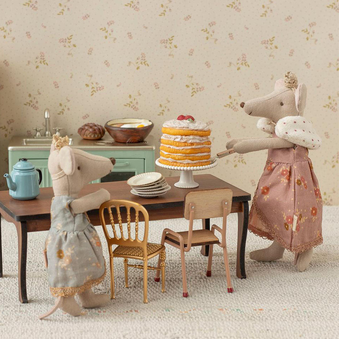 Twee Maileg muizen in een miniatuurkeuken, één serveert taart en de ander staat bij een theepot.