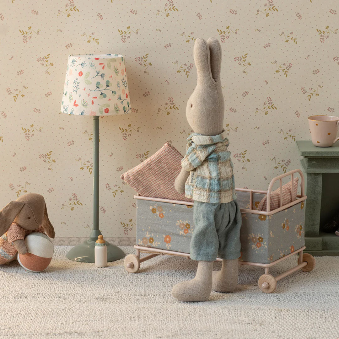 Een Maileg konijn pop staat naast het poppenreisbed met bloemenpatroon in een speelkamer met bloemenbehang.
