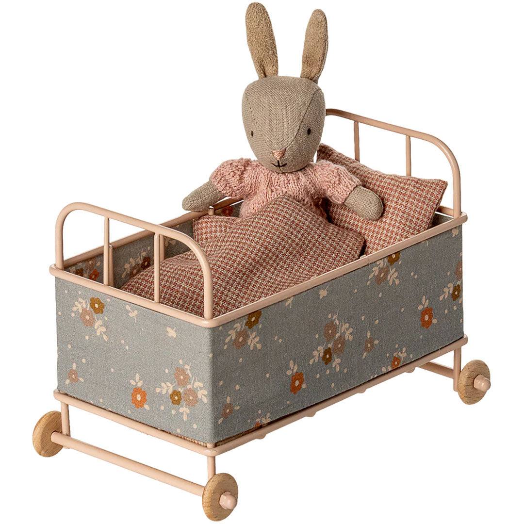 Maileg poppenreisbed met bloemenpatroon en een Maileg konijn pop in een roze trui die erin ligt, bedekt met een deken.