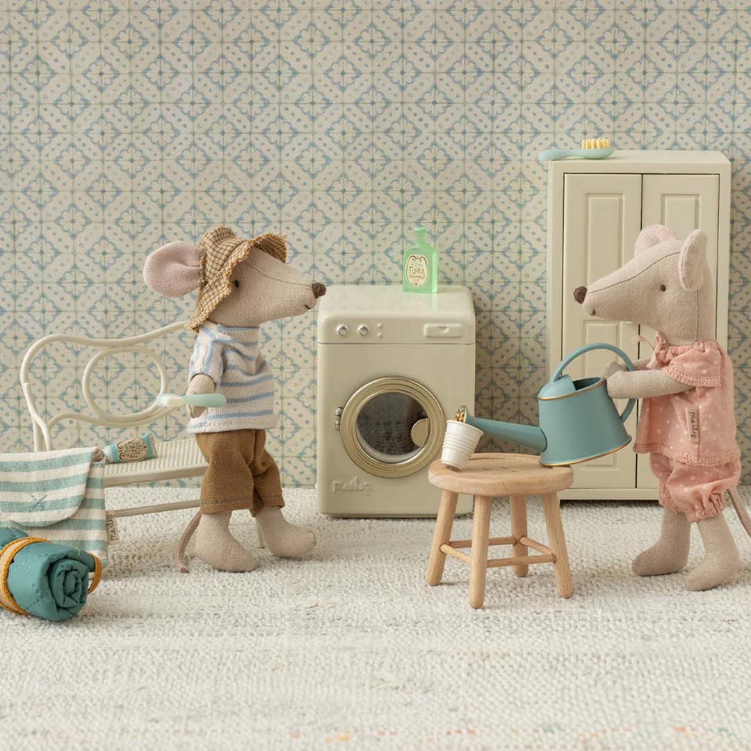Twee Maileg muizenpoppen in een badkamer met de poppenverzorgingsset en een wasmachine.