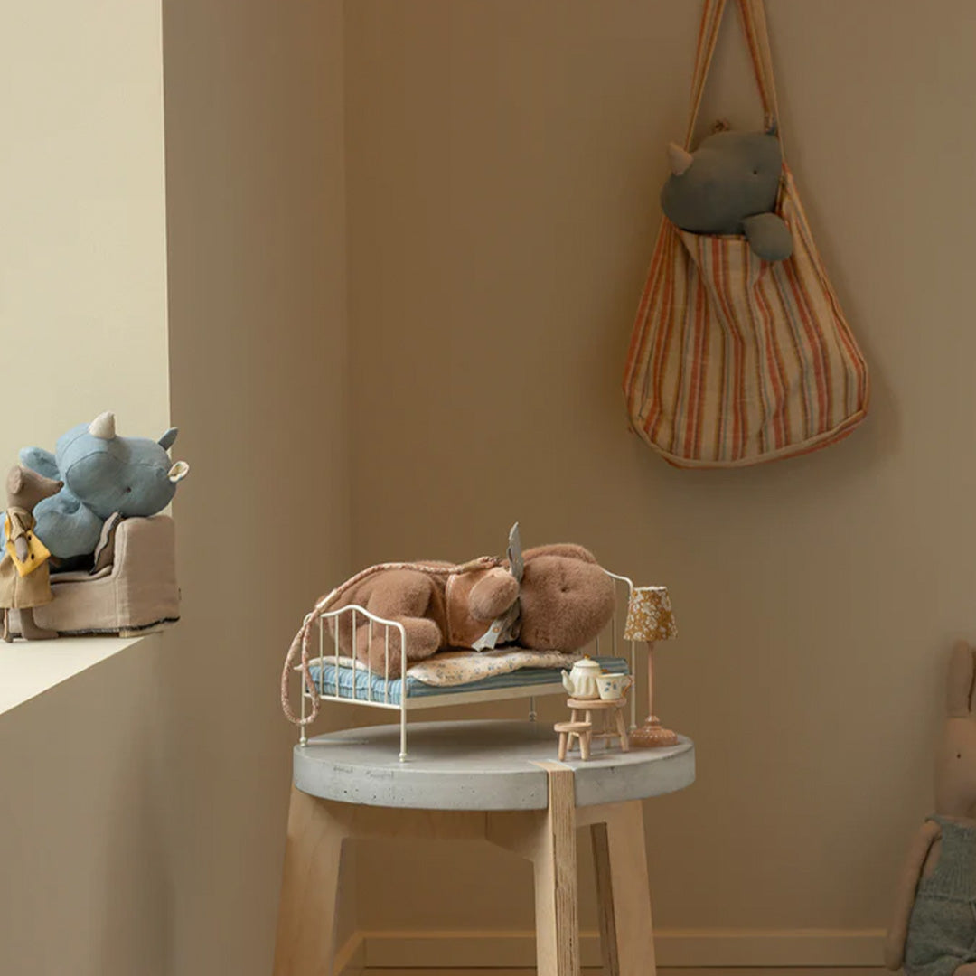 Maileg speelscène met slapende knuffelkonijn in een bedje en een gestreepte tas aan de muur.