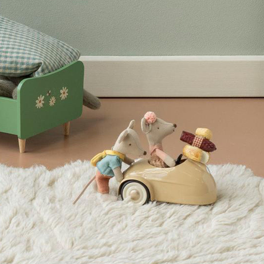 Twee Maileg muizenpoppen met de beige speelauto, waarvan één achter het stuur zit en de ander ernaast staat, op een wit kleed.
