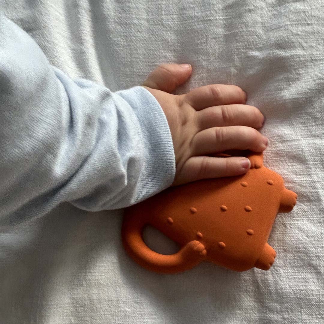 Een babyhandje houdt het Maison Petit Jour bijtspeelgoed in de vorm van een oranje beer vast.