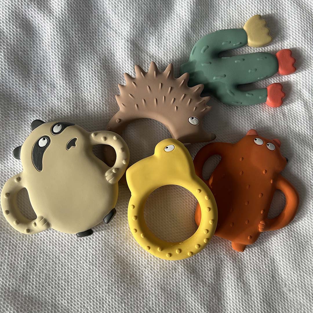 Een collectie Maison Petit Jour bijtspeeltjes, waaronder een beer, panda, egel, cactus en een gele ring, op een witte ondergrond.